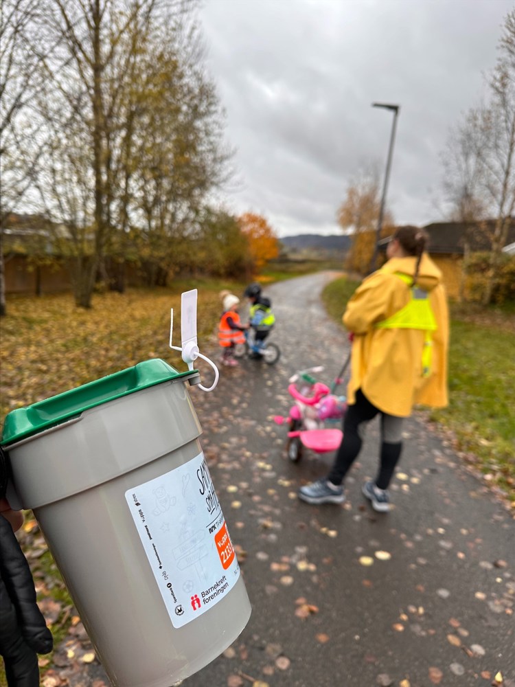 En bøsse er i forgrunnen og to barn og en kvinne er i bakgrunnen ute en høstdag.